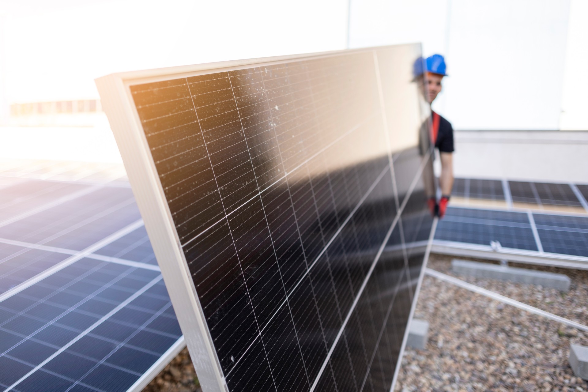 A worker on the roof next to the solar panels carrying a panel, sustainable living.